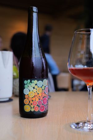 Artistically designed wine bottle with colorful bubble pattern and glass of red wine on wooden table.