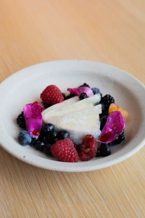 Fresh berries and edible flowers arranged around white cheese on ceramic plate.