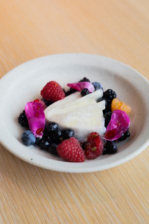 Mixed berries and pink flower petals surrounding white cheese on rustic ceramic dish.