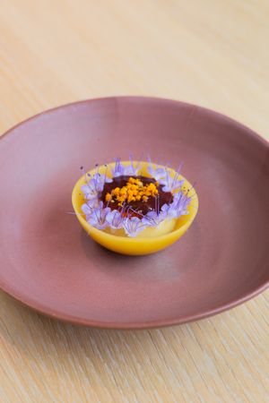 A chocolate dessert with purple flower garnishes served in a yellow bowl on a brown ceramic plate.