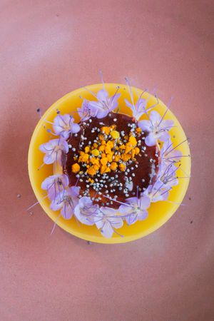 Artistic dessert presentation with chocolate, orange segments and purple flowers in yellow serving bowl.