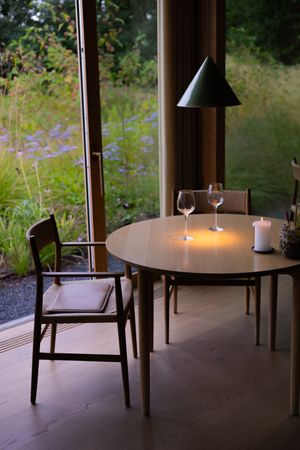 Minimalist dining table with candles and wine glasses beside large windows with garden views.