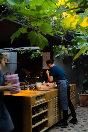 Restaurant kitchen staff working at wooden prep station under hanging plants.