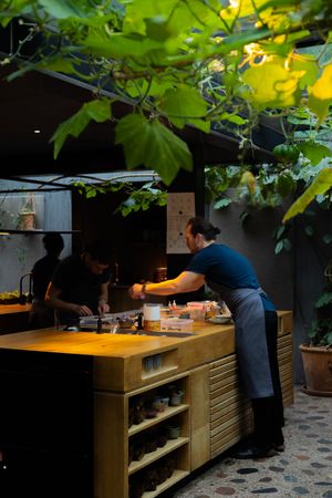 Restaurant staff work behind a wooden counter beneath hanging vines in a dimly lit space.