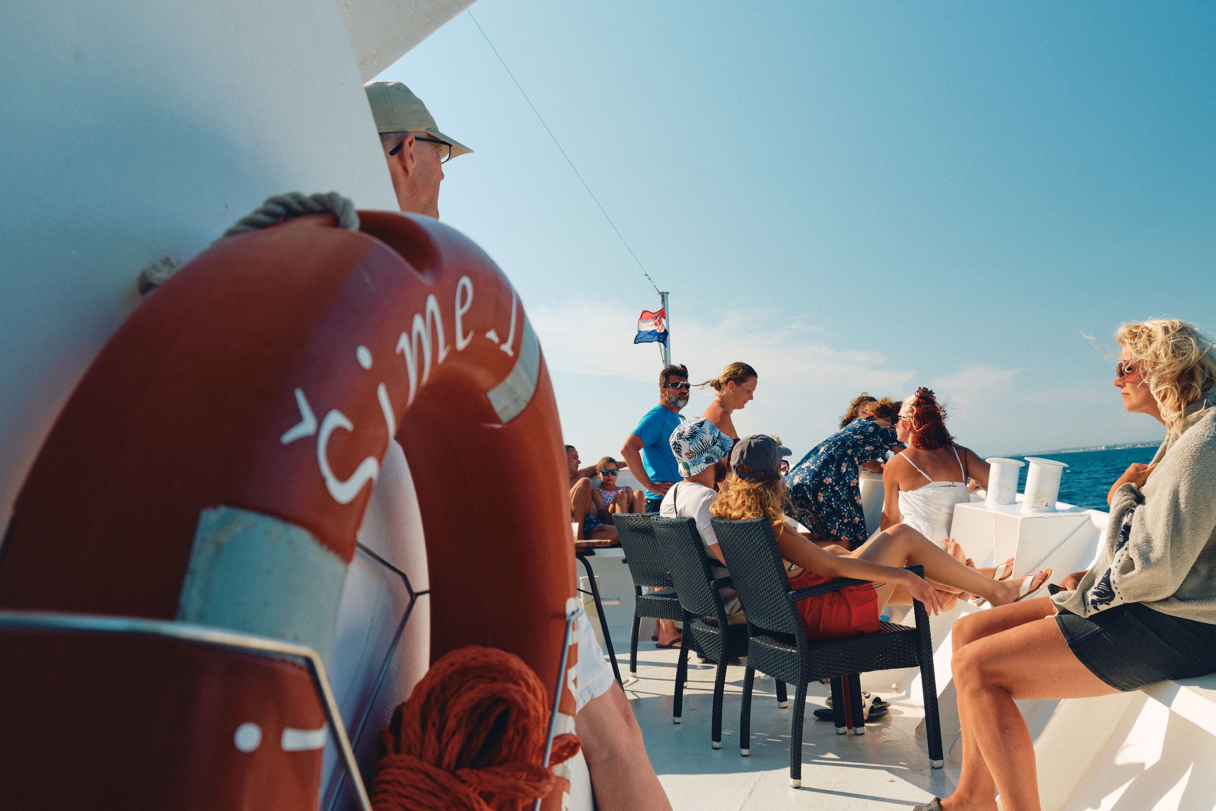 Red life preserver and passengers relaxing on boat deck during Mediterranean cruise.