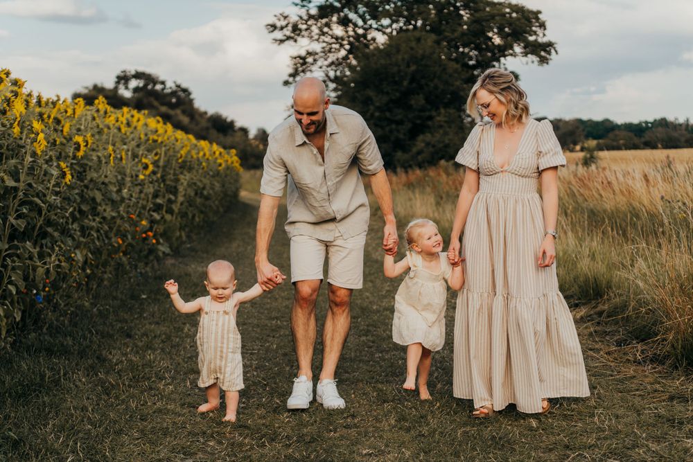 People walking together on a dirt path alongside a field of yellow flowers during golden hour. Family Photoshoot. Writtle Sunflowers.