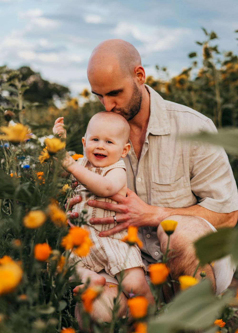 A tender moment shared in a flower field filled with vibrant orange blooms on a sunny summer day.  Family Photoshoot. Writtle Sunflowers.