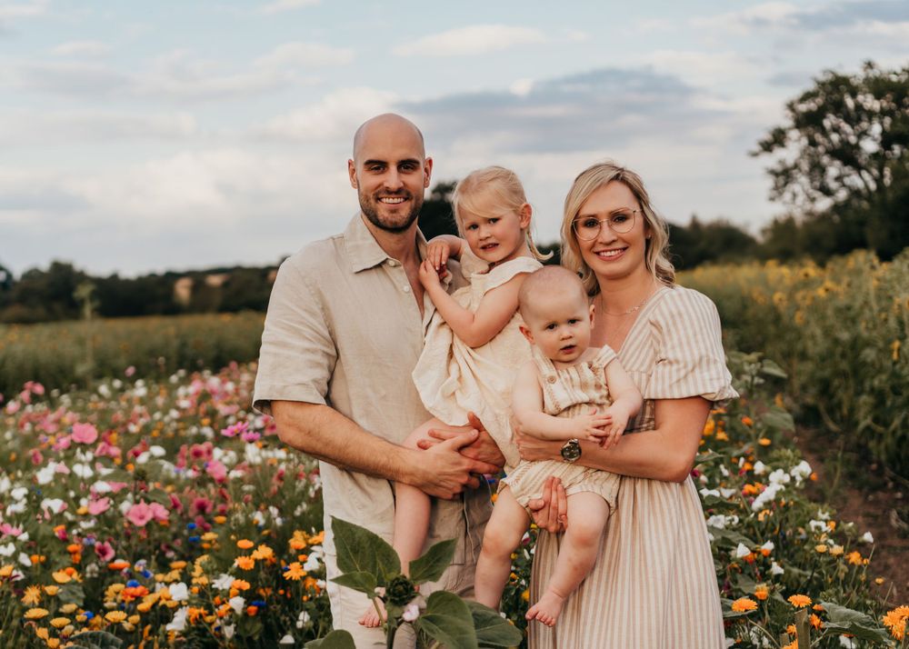 A family poses together in a vibrant wildflower field at sunset with colorful blooms of pink and yellow flowers.  Family Photoshoot. Writtle