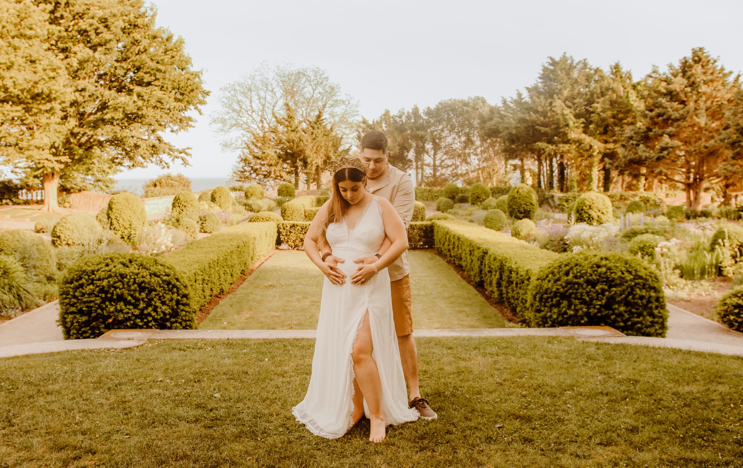 A couple shares an intimate moment in a formal garden with manicured hedges and golden sunlit atmosphere in Waterford, Connecticut.