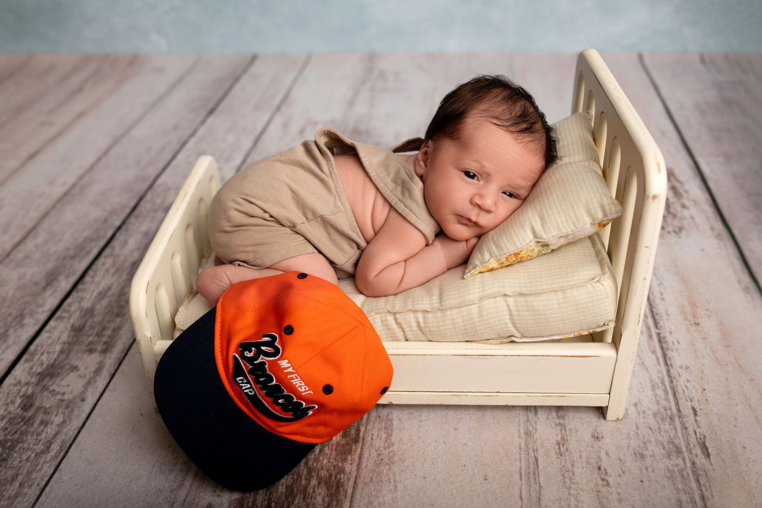 Sleeping baby in cream-colored bed with orange Halloween pumpkin decoration on wooden floor.