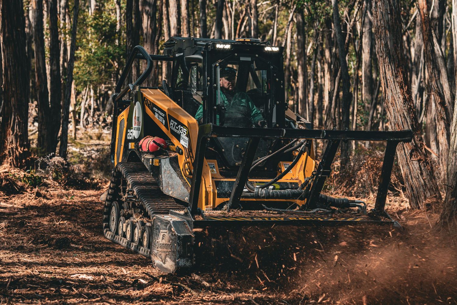 Heavy equipment operating in dense forest clearing with flying debris.