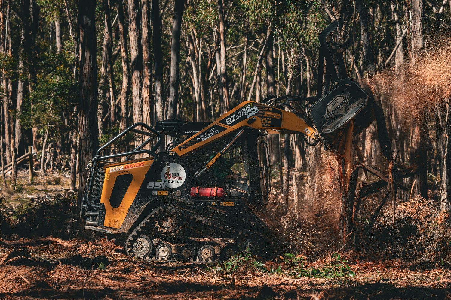 Industrial machinery working in wooded area with dirt and debris clouds.