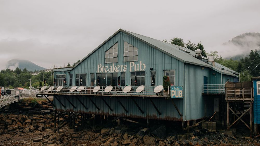 A panoramic view of a rustic seafood pub with teal-colored exterior situated along a coastal shoreline.