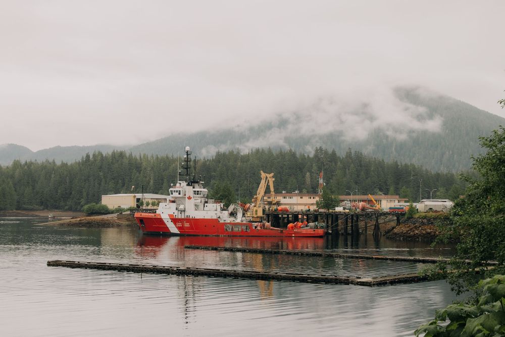 Red Coast Guard vessels docked at a misty harbor in Alaska with fog-covered mountains in the background.