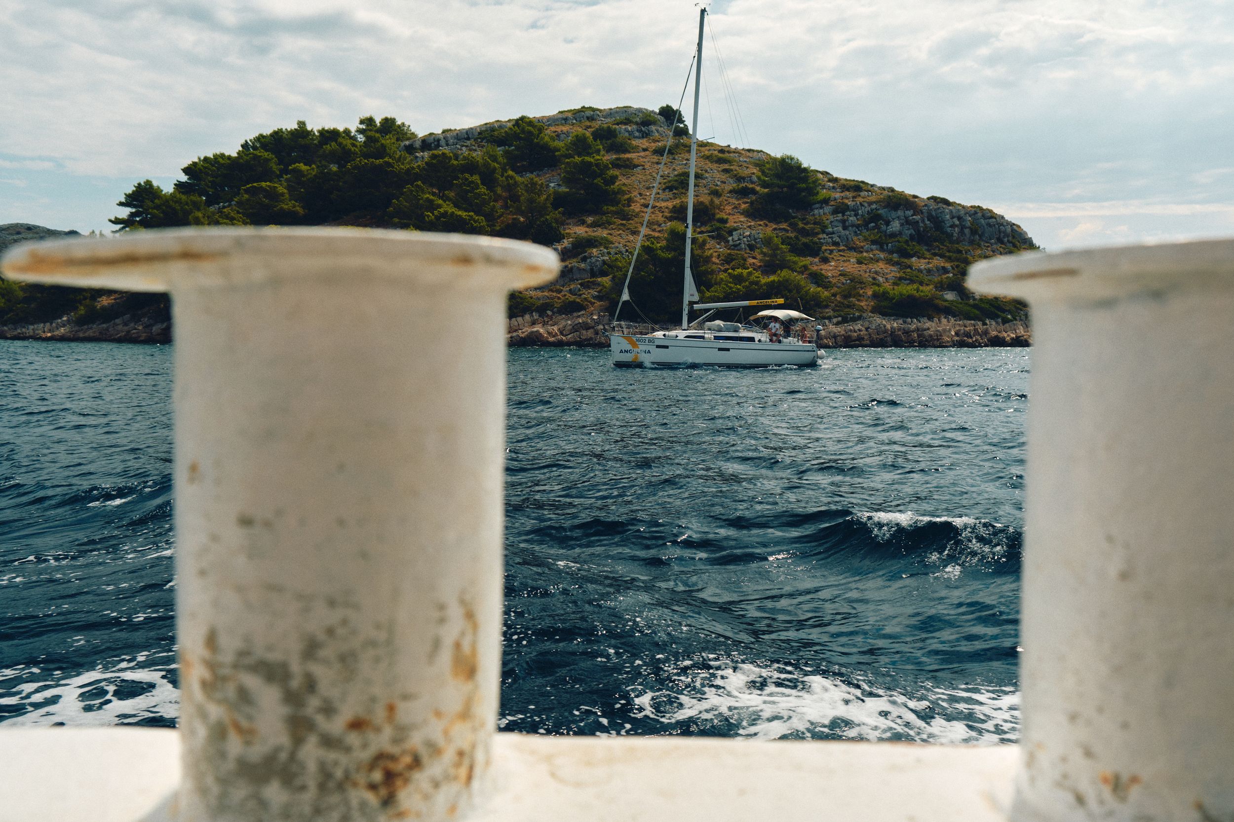 Sailboat anchored near an island viewed between two white boat posts.