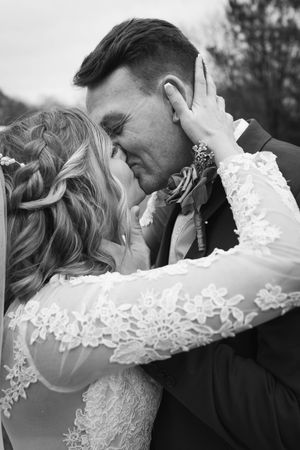 Black and white wedding photo of bride and groom sharing a romantic kiss, bride in lace dress embracing groom.