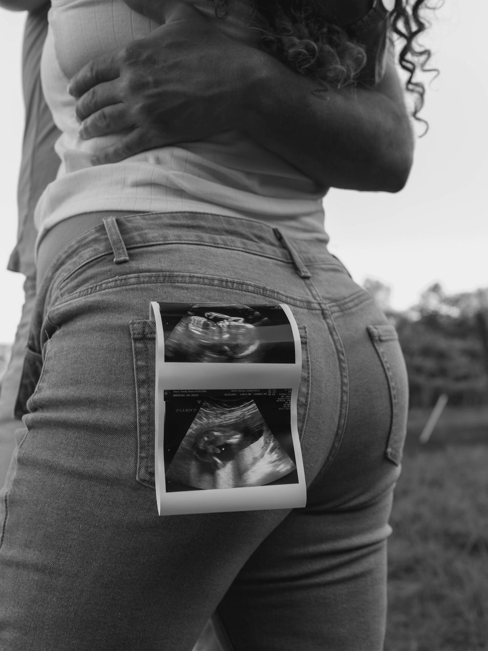 Series of ultrasound photos tucked into the waistband of jeans showing pregnancy announcement.