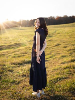 Maternity photography session in a sunlit field wearing navy dress.