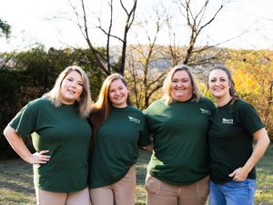 Group wearing matching green shirts posing together outdoors in autumn setting.