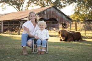 Family photoshoot on blanket with farm animals and barn in background.