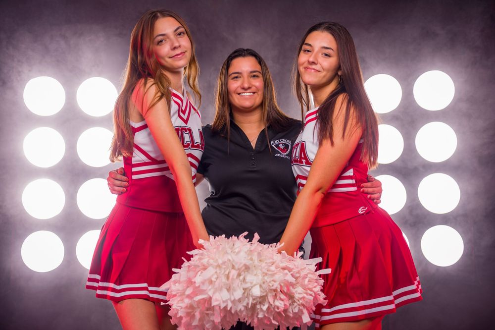 Three cheerleaders in red uniforms pose with white pom poms against bright spotlights in the background.