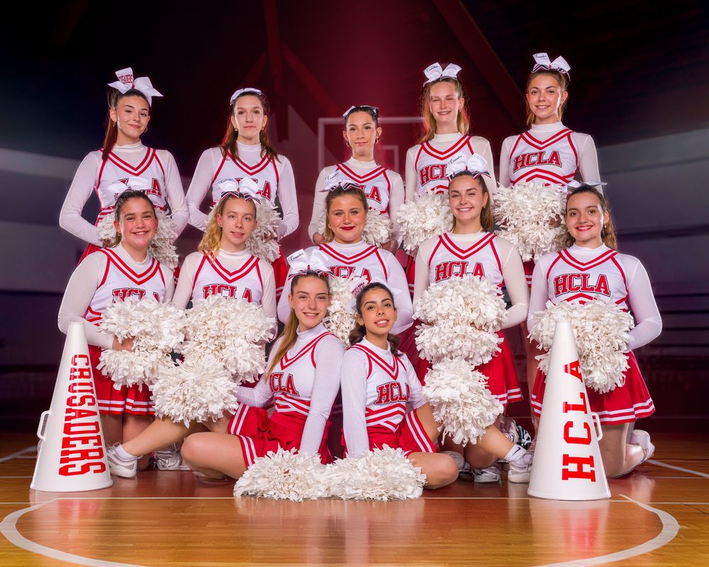 College cheerleaders in red and white uniforms pose together in a panoramic sports team photo on a basketball court.