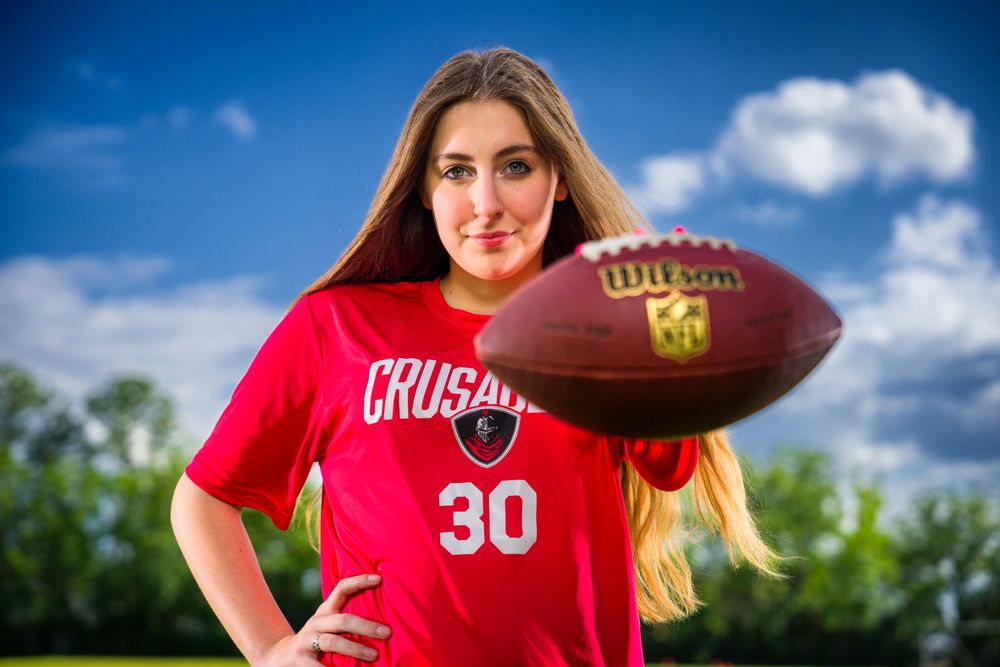 Athlete in red jersey number 30 holds a football while posing outdoors against blue sky with clouds.