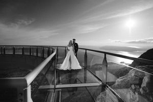 A couple shares a romantic moment on a glass skywalk observation deck at sunset in black and white photography.