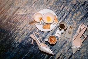 High angle view of breakfast with soft boiled eggs, espresso, and elegant beige high heel shoes on rustic wooden surface.