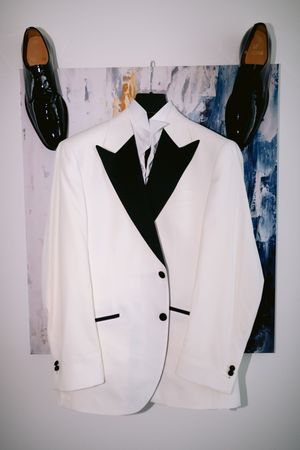 A white formal dinner jacket with black lapels shown from different angles against a blue and white background.