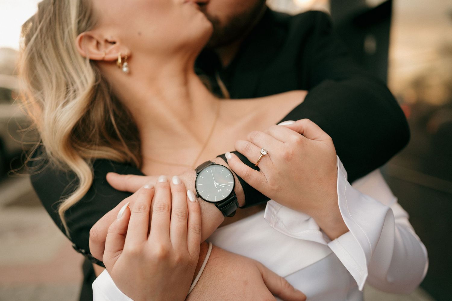 Close-up shot of hands embracing with a wristwatch detail in romantic golden light.