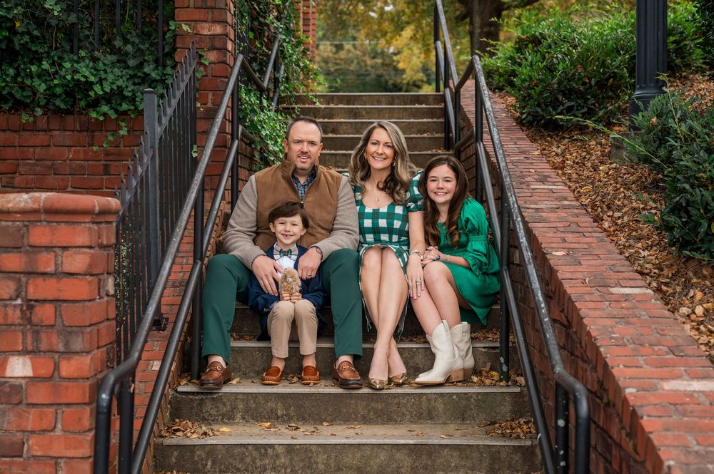 People wearing green sit together on outdoor brick stairs during a casual family photo session.