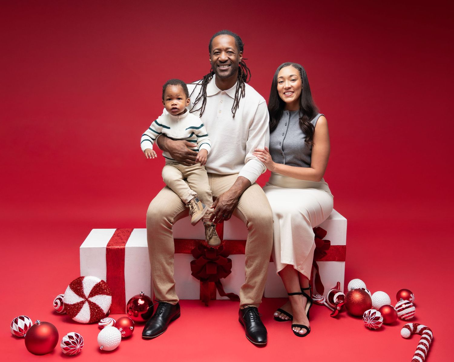 A group of people sitting on a red backdrop wearing white outfits and striped socks in a playful studio photoshoot.