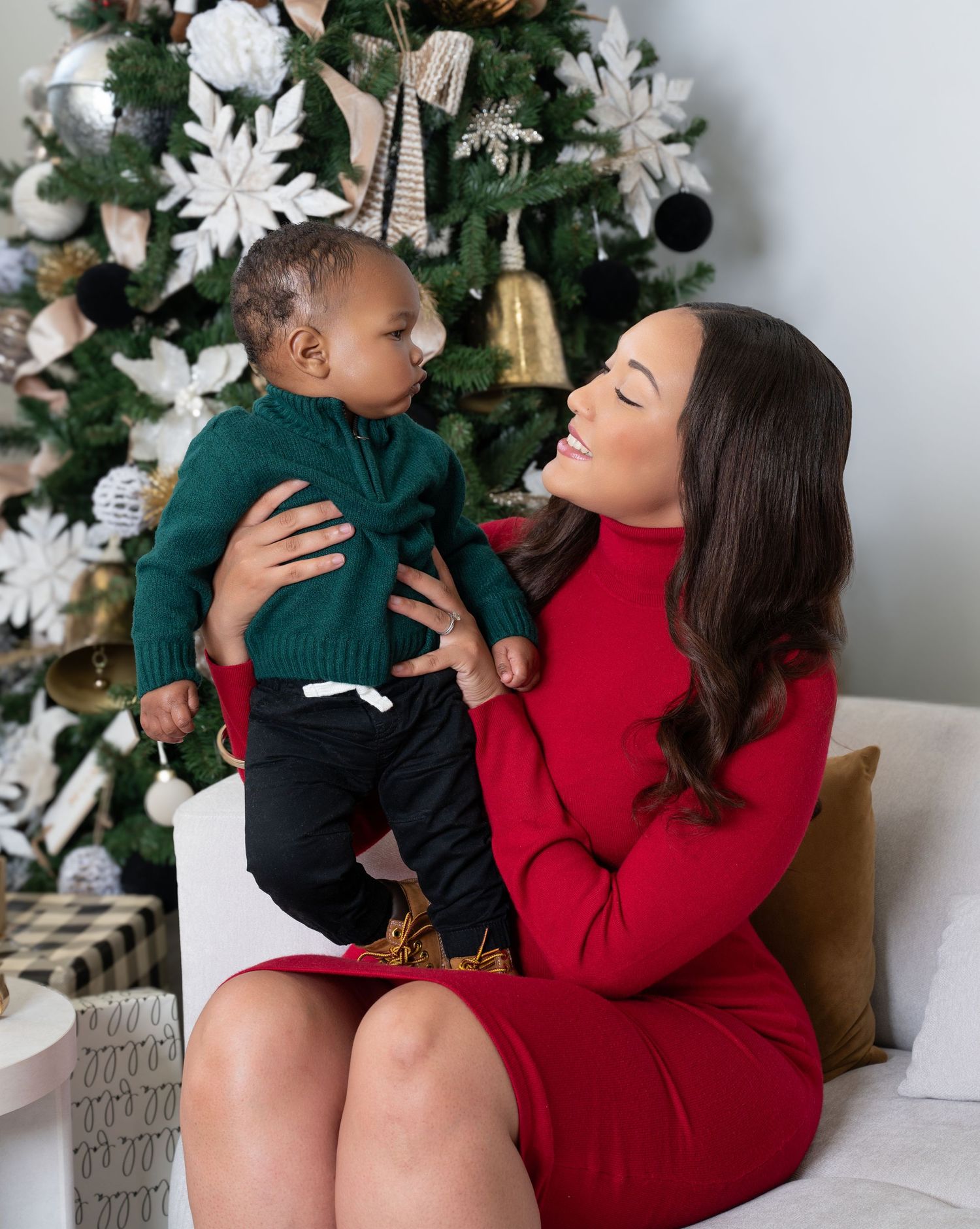 Festive holiday scene with decorated Christmas tree, wrapped presents, and family moment in red and green attire.