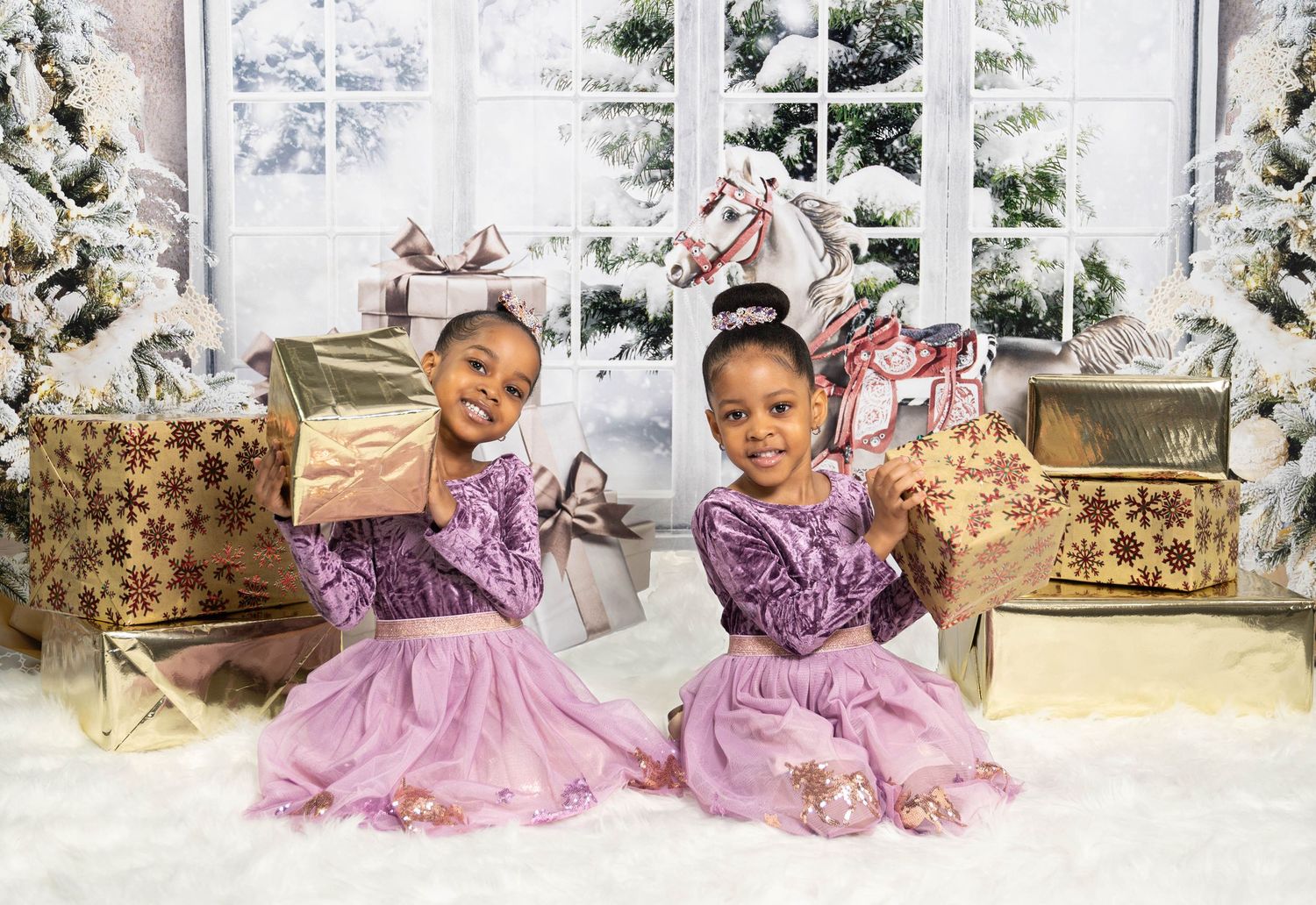 Two young children in matching purple dresses pose with gold presents in a Christmas studio setting.
