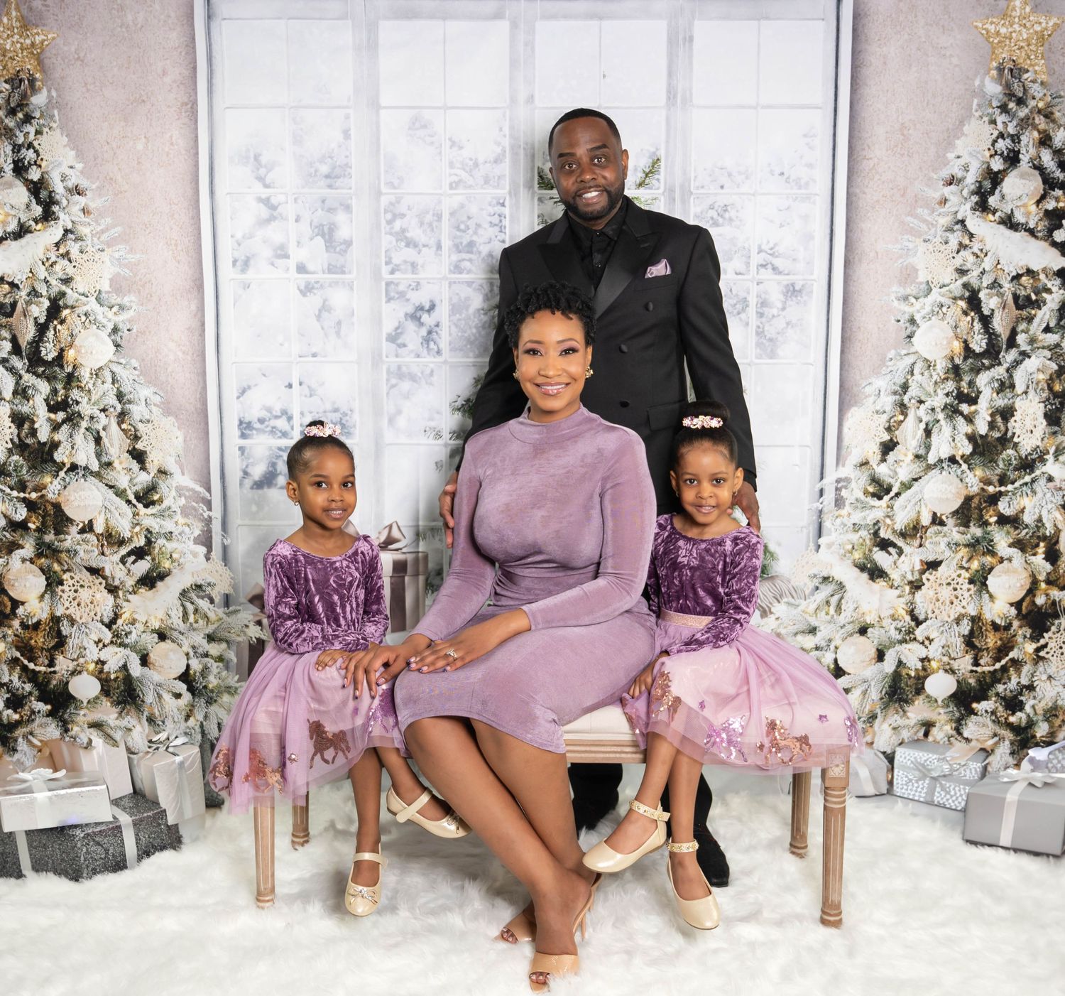 Family portrait in front of Christmas trees with matching purple and mauve outfits.