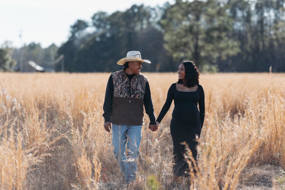 Two people holding hands while walking through a golden wheat field on a sunny day.
