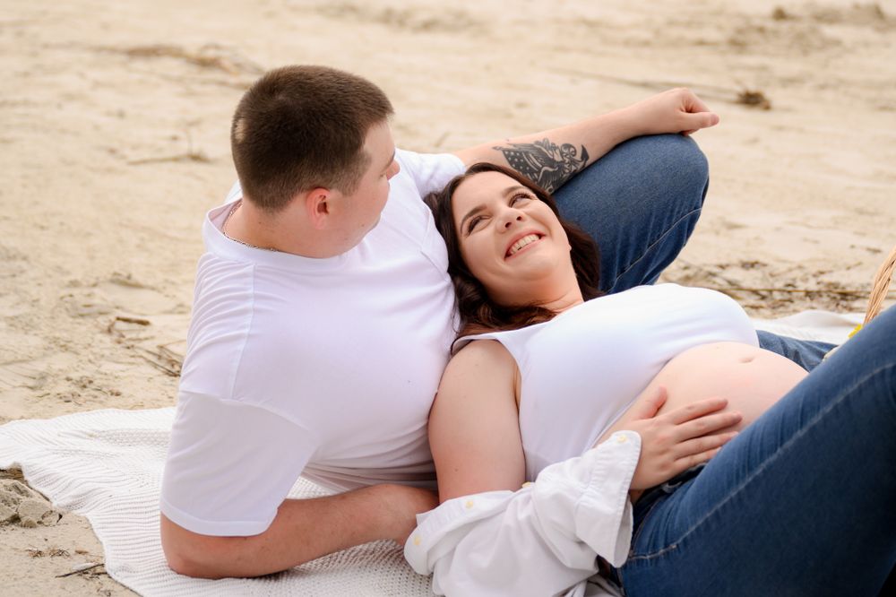 Intimate maternity beach photoshoot on white blanket at sunset.