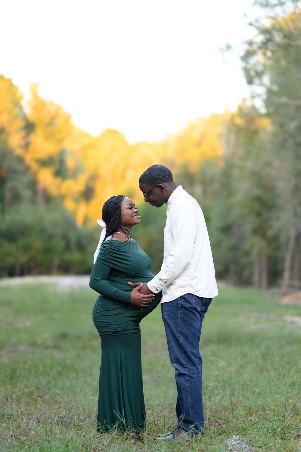 A couple shares an intimate moment outdoors at sunset, with the expectant mother wearing an elegant emerald green dress.