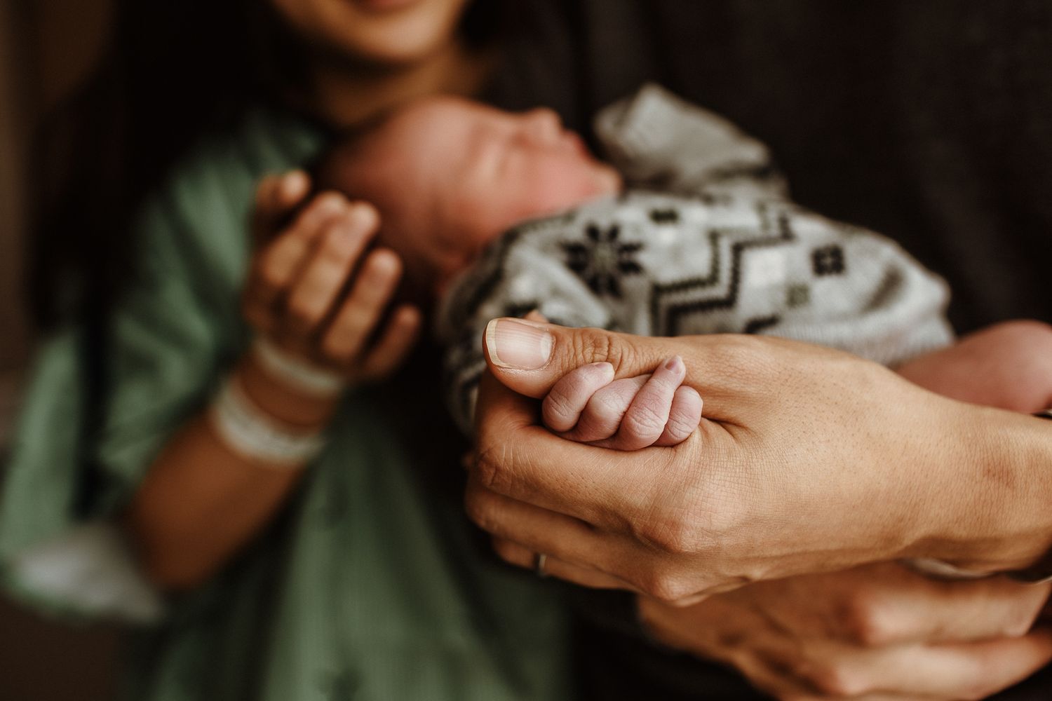 Medical professional's hands holding and examining newborn baby's tiny hand.
