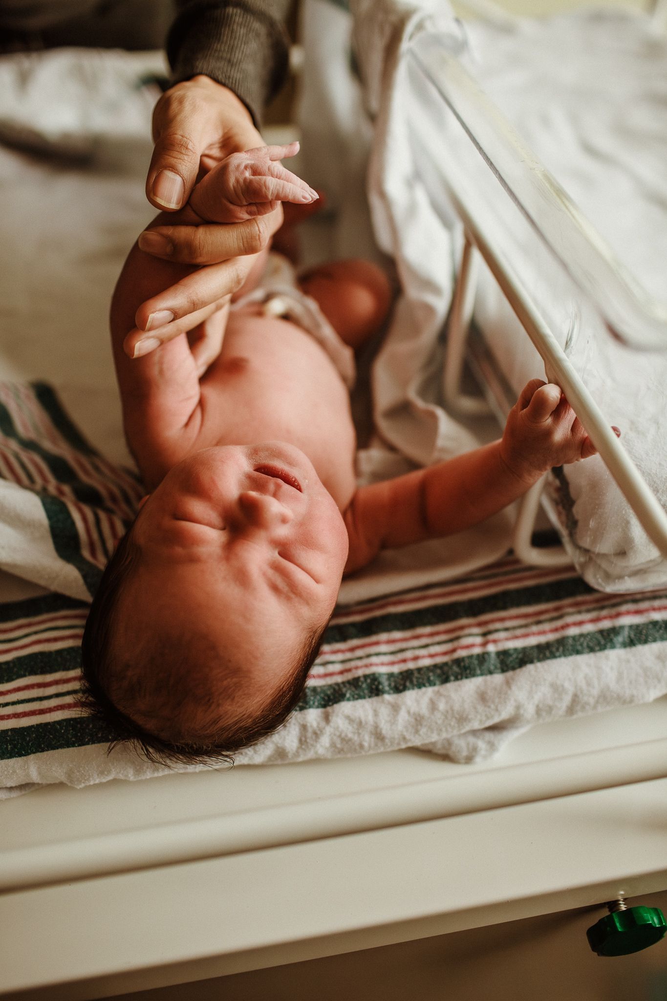 Close-up shot of a newborn baby resting on striped blanket during medical examination.