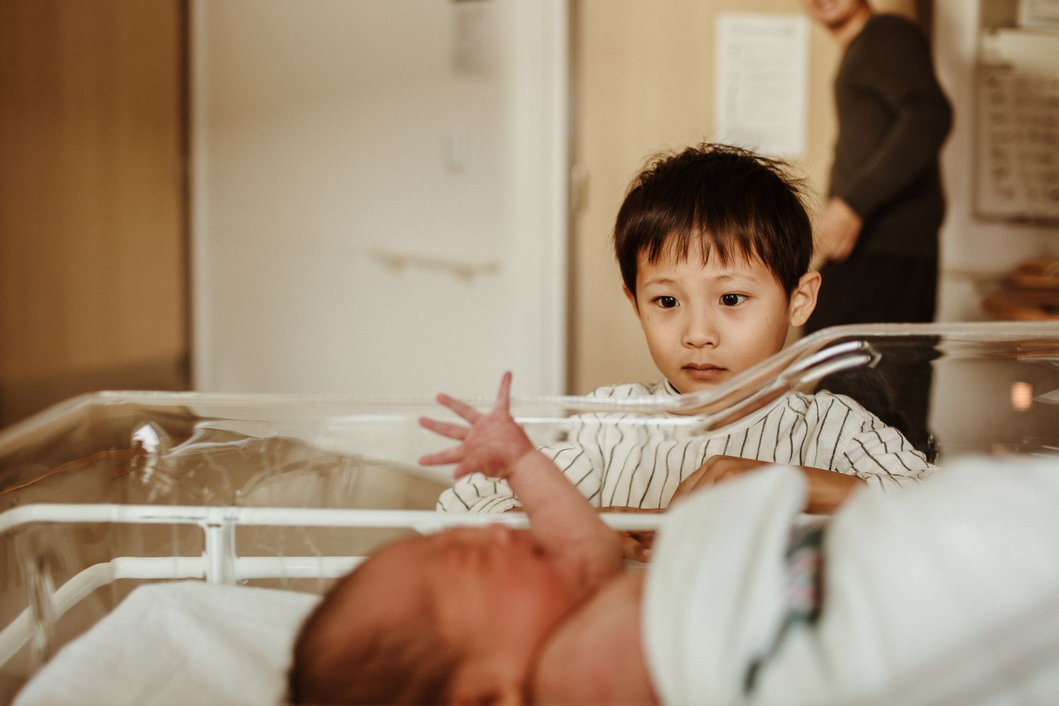 Family watching newborn in hospital incubator through clear plastic.