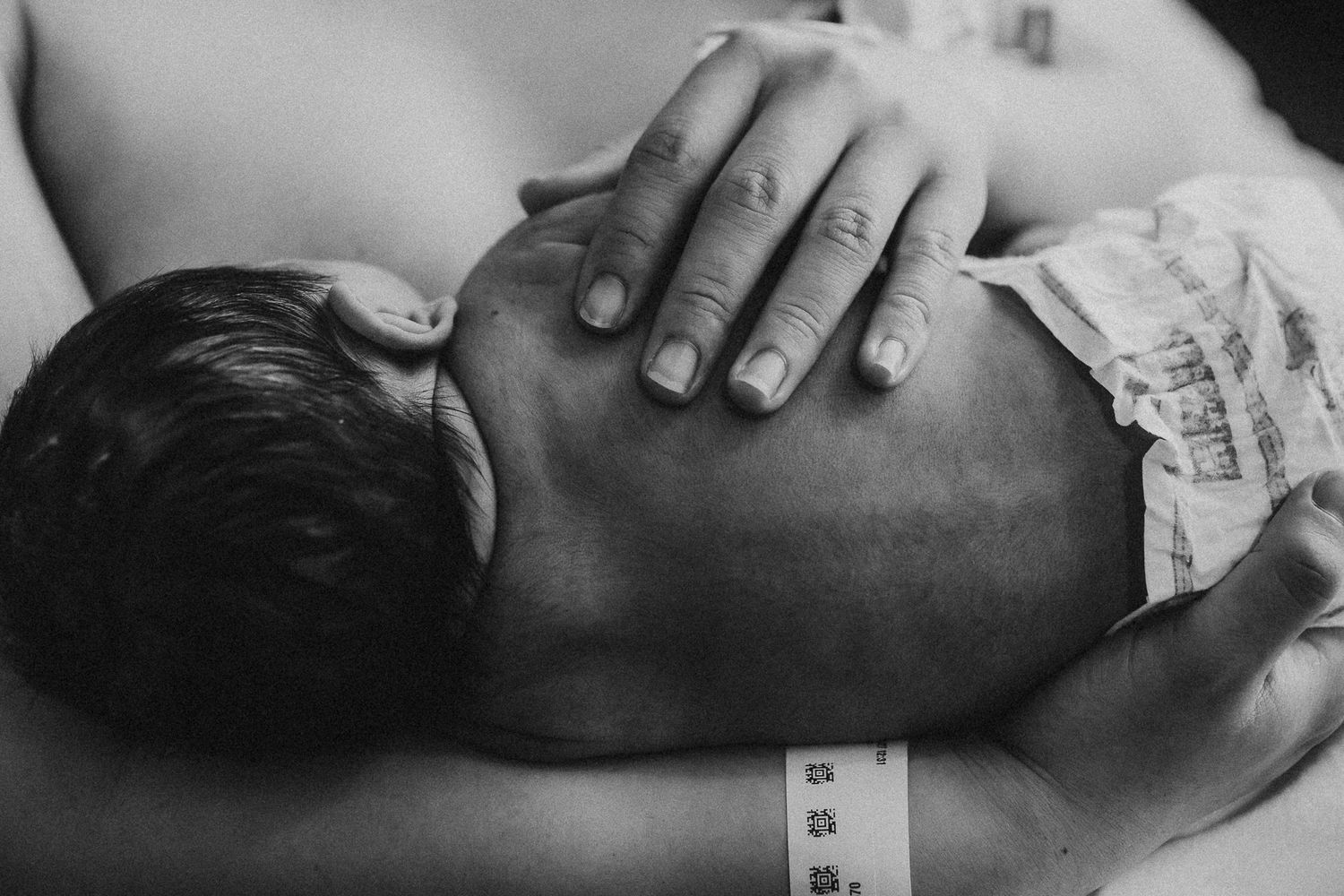 Black and white image of gentle hands examining newborn in hospital.