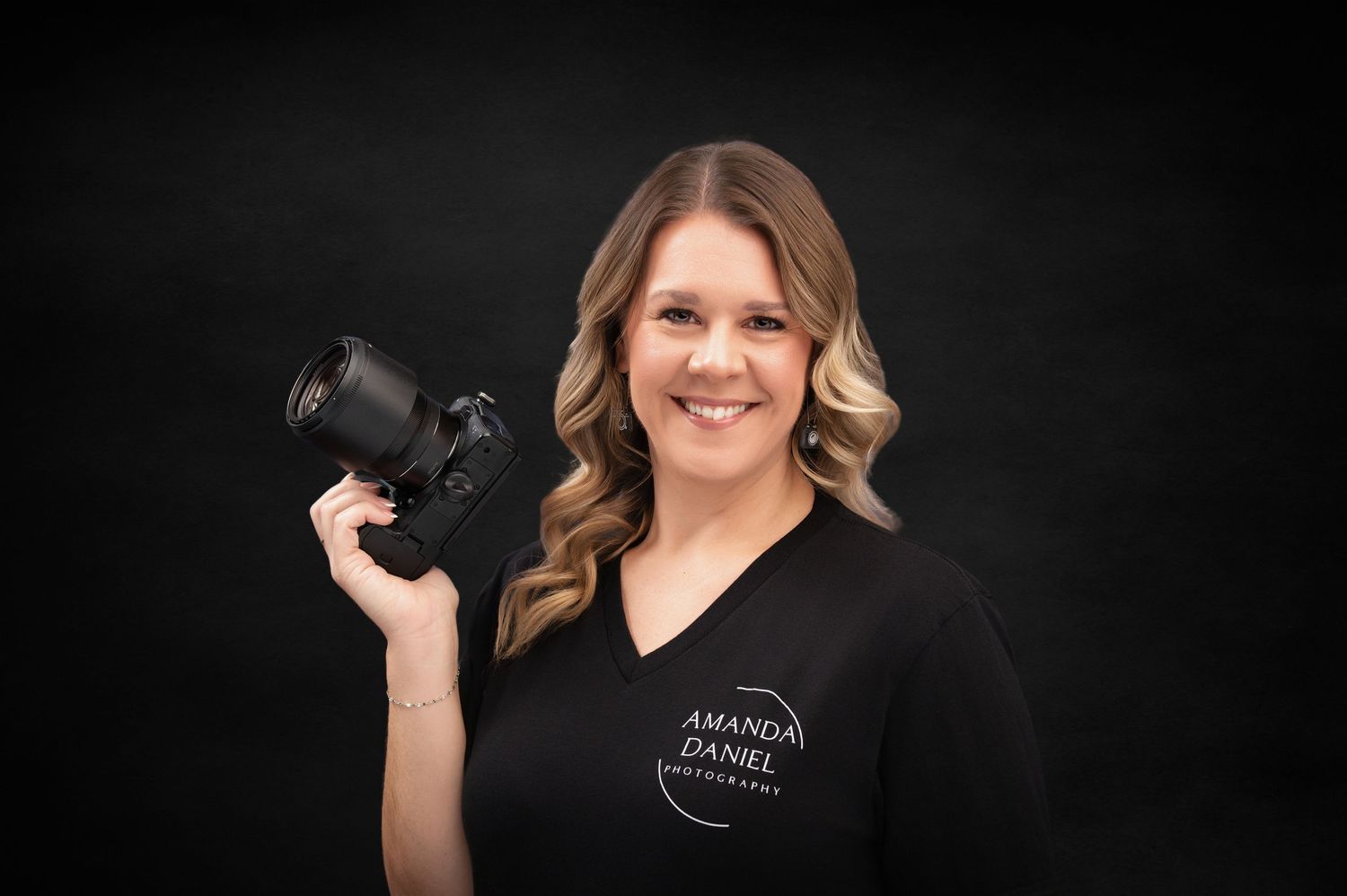 Professional photographer in black v-neck shirt holding DSLR camera against dark background.