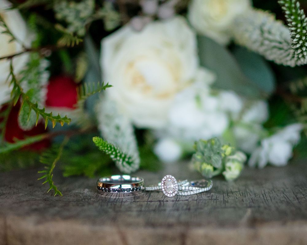 Wedding rings nestled among white roses and greenery on a wooden surface.