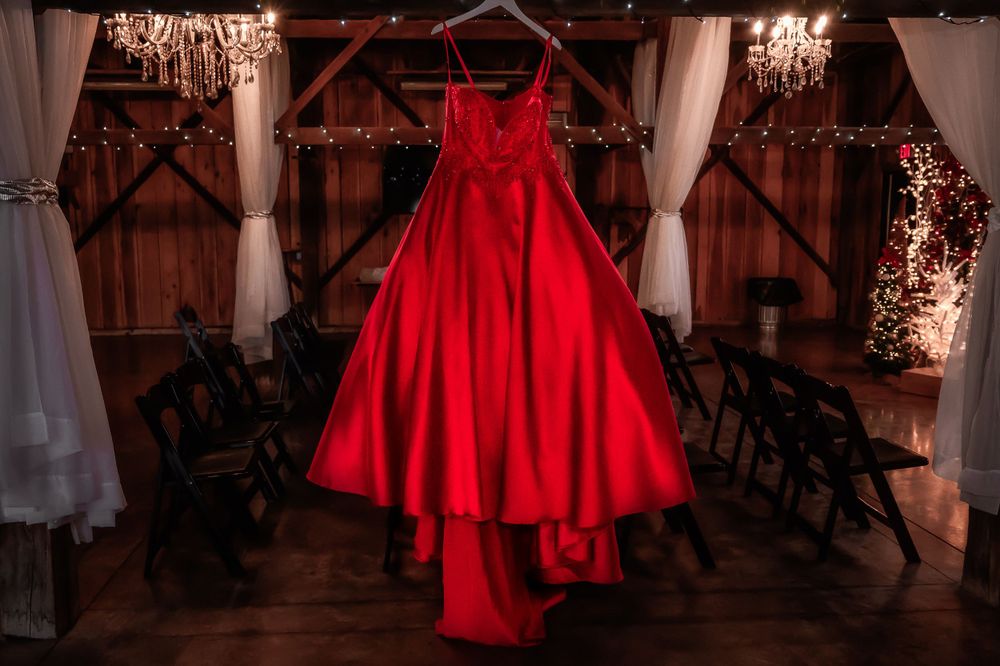 A vibrant red wedding gown hangs dramatically in a rustic venue with string lights.
