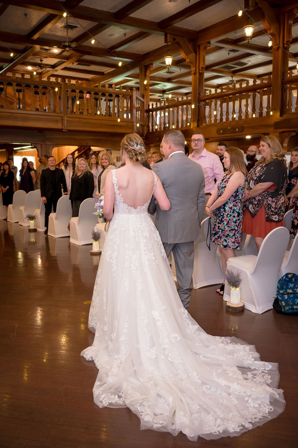 Elegant reception venue with wooden beams and chandeliers as bride walks through in lace gown.
