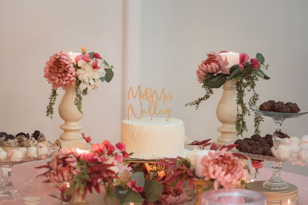 Elegant dessert table with white cake, pink flowers and decorative stands.