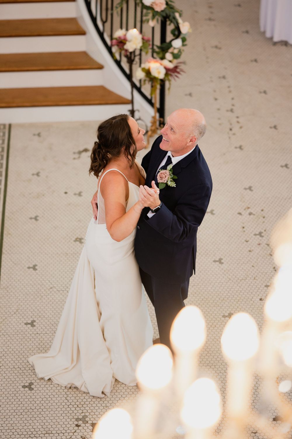 Couple dancing in elegant attire on carpeted stairs with floral decorations.