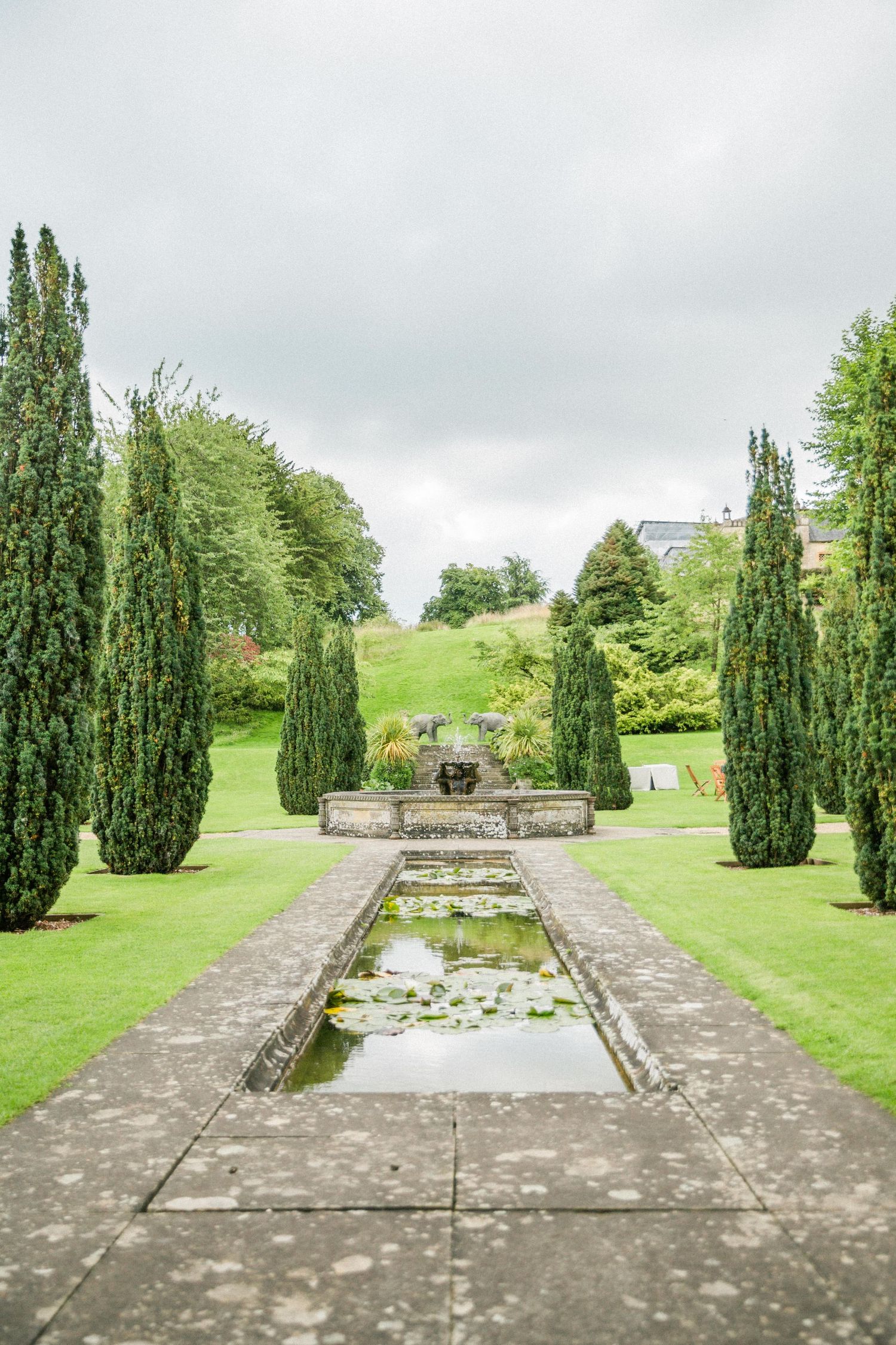 Formal garden path with cypress trees and reflecting pool leads to ornate stone fountain in lush green landscape sezincote house cotswolds